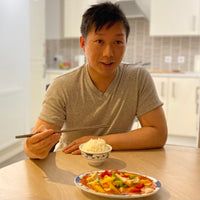 Vincent sat on a dinner table holding chopsticks with a bowl of rice and chinese meal placed on the table